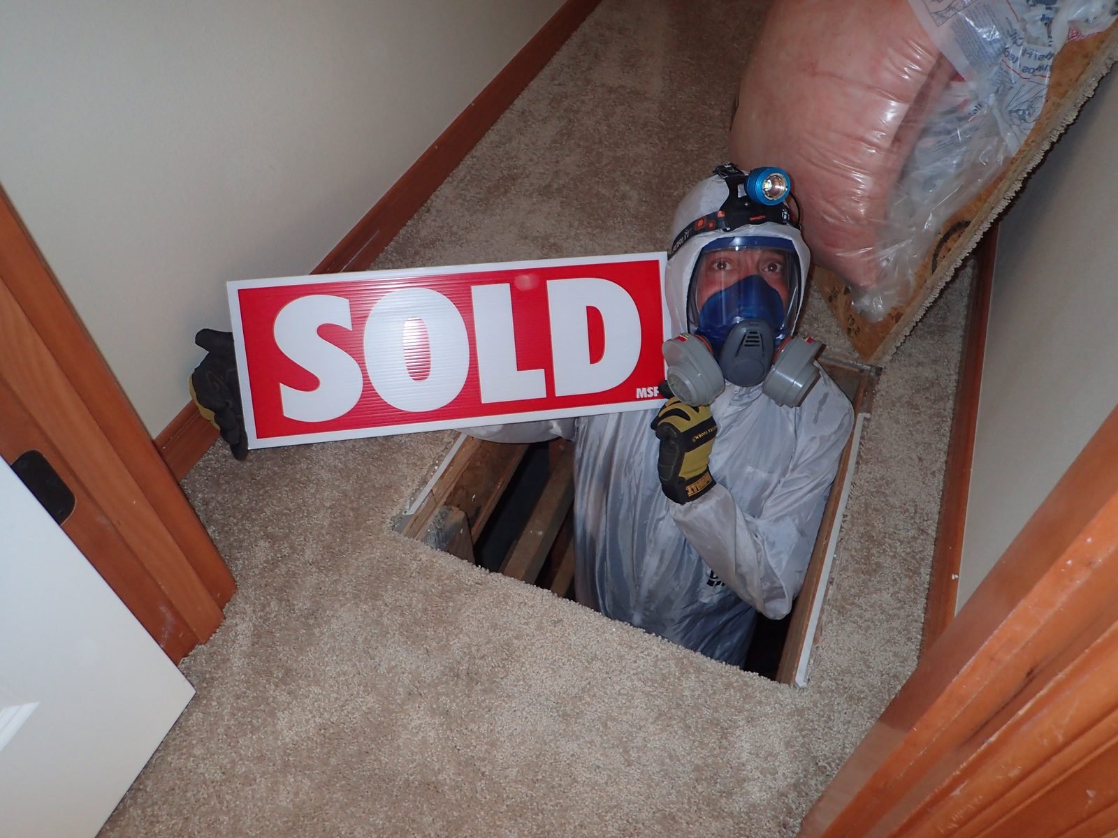 Bryan Mize emerging from crawlspace holding a SOLD sign